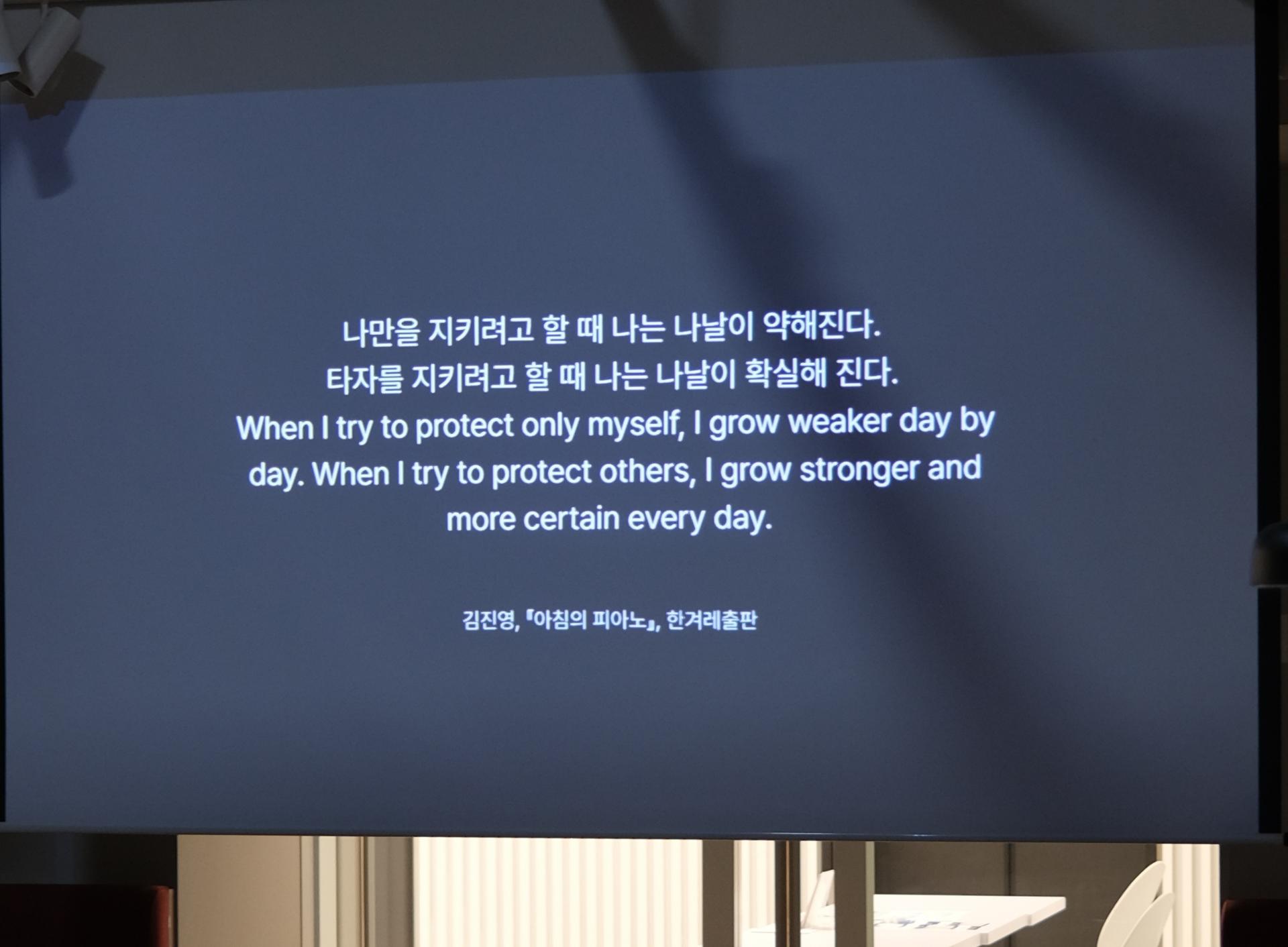 “스크린에 ‘나만을 지키려고 할 때 나는 약해진다. 타자를 지키려고 할 때 나는 나날이 확실해 진다’는 글귀와 영어 번역이 함께 보인다.