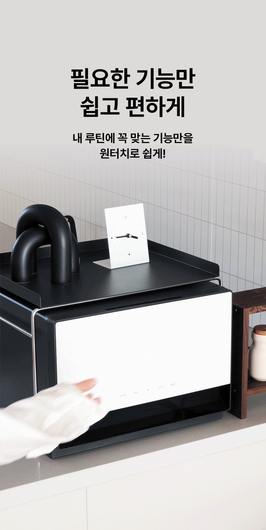 사선 위치로 다크 그레이 바디에 오프화이트 컬러의 픽셀 젖병소독기가 맘마존 트레이 하부에 놓여져있고 맘마존트레이 상부에는 오브제와 시계가 놓여져있는