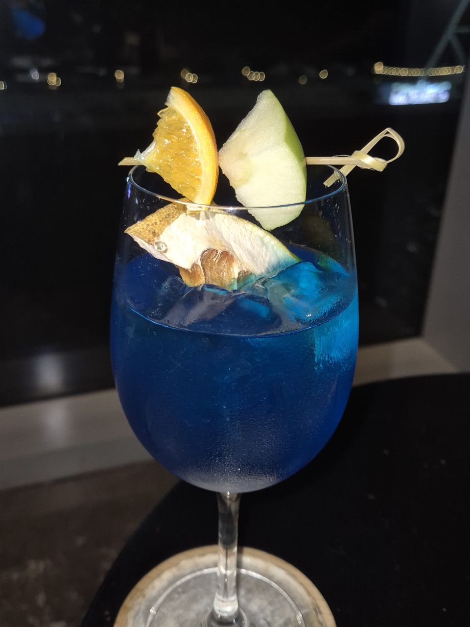 마닐라의 밤 야경을 배경으로 장식된 푸른색 시그니처 칵테일 한 잔