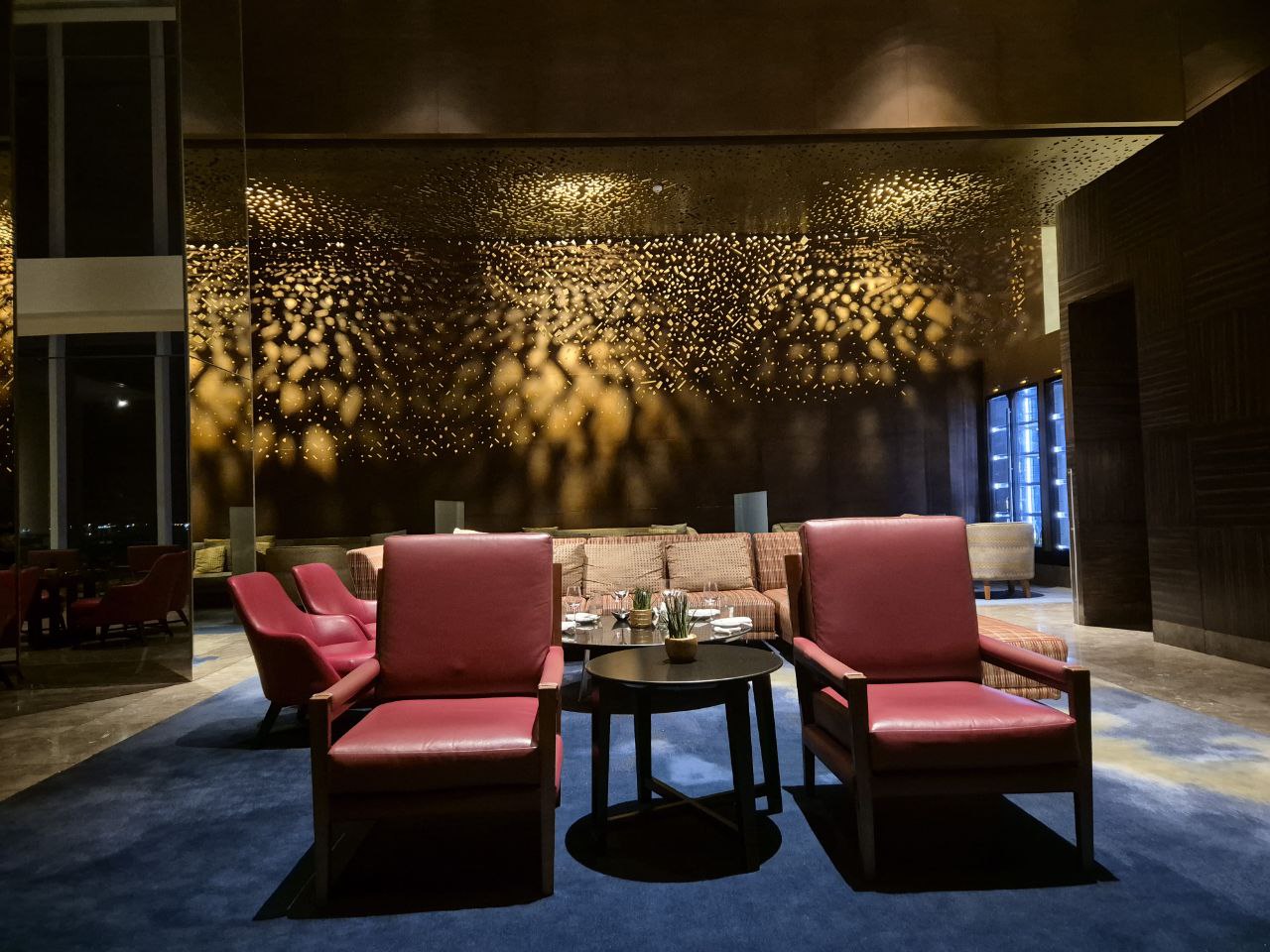 고급스러운 황금빛 조명과 붉은 소파가 돋보이는 콘래드 호텔 C 라운지 인테리어
