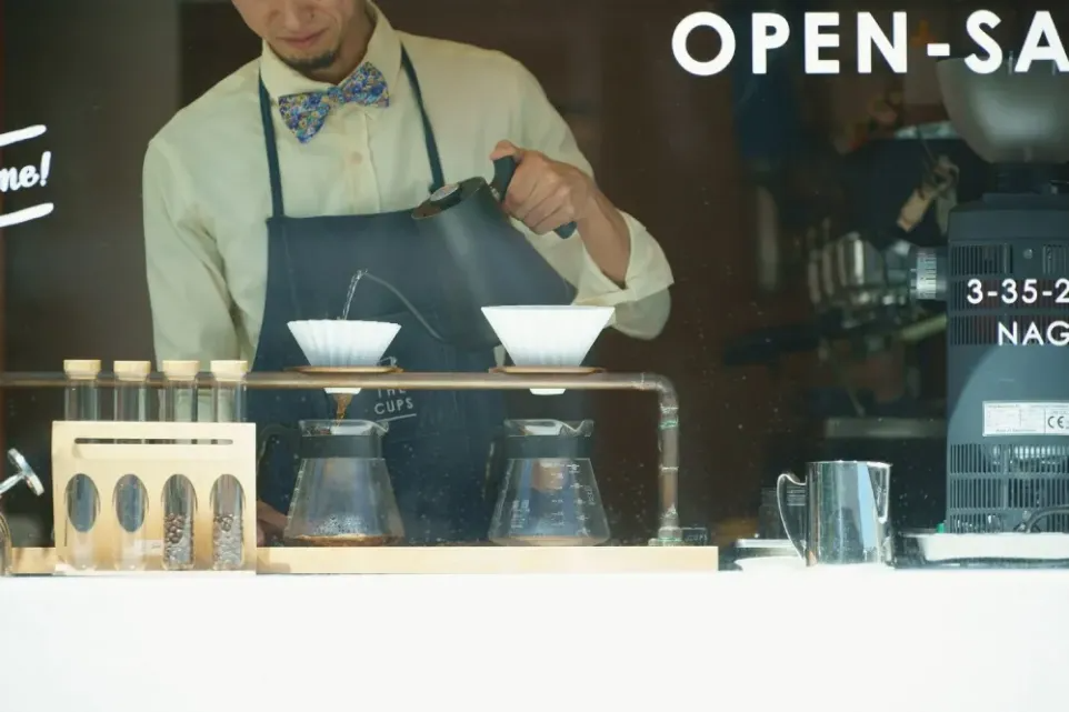 A barista prepares two pour overs in a coffee shop.