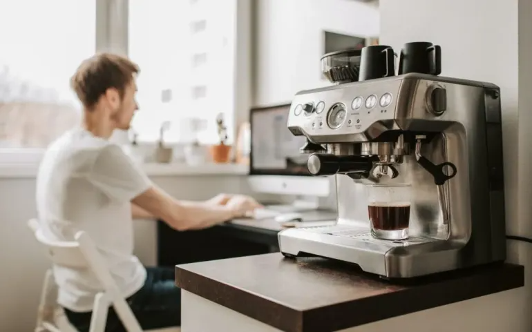 A man works on his computer alongside a home espresso machine.