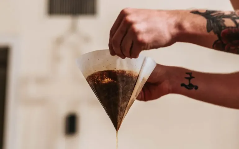 A barista allows coffee to drip from a paper filter.