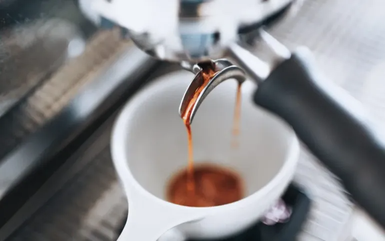 Espresso pours out of a portafilter on an espresso machine.