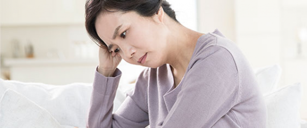 소파에 앉아 머리를 짚고 있는 여성
